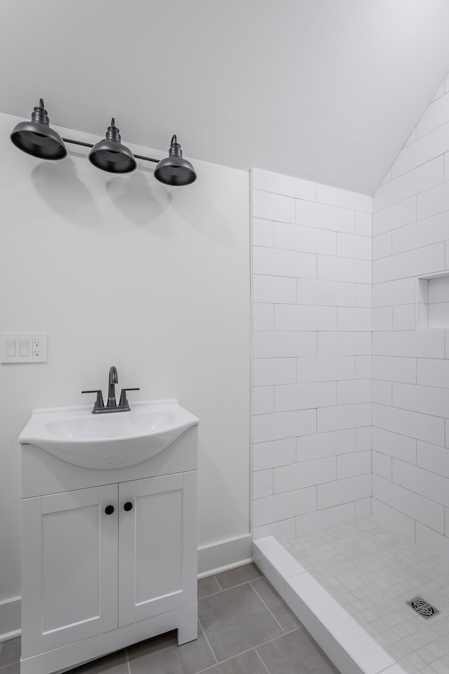 bathroom featuring tile patterned flooring, vanity, lofted ceiling, and tiled shower