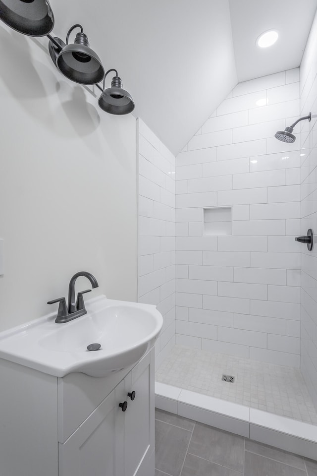 bathroom with vanity, tile patterned flooring, vaulted ceiling, and tiled shower