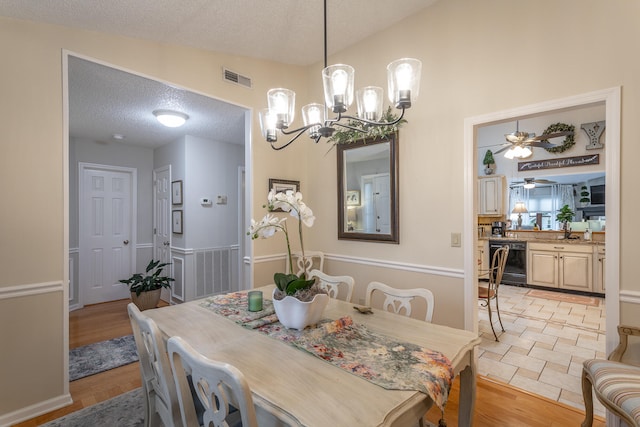 dining room with light hardwood / wood-style floors, a textured ceiling, lofted ceiling, and ceiling fan with notable chandelier