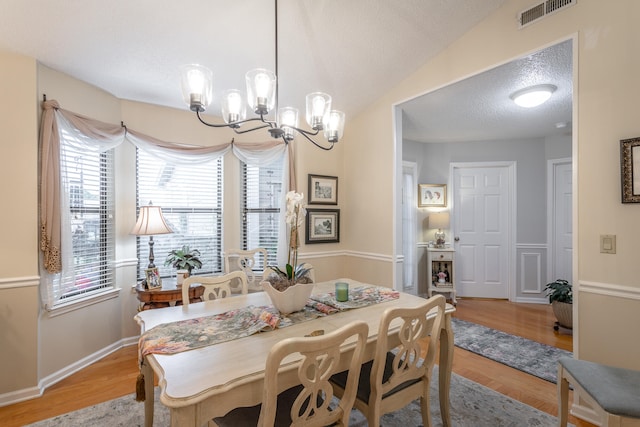 dining area with light hardwood / wood-style floors, a notable chandelier, a textured ceiling, and lofted ceiling