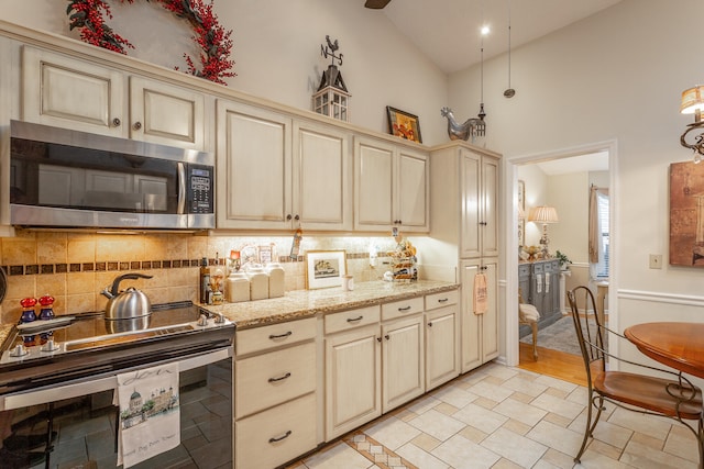 kitchen featuring decorative backsplash, cream cabinetry, stainless steel appliances, and high vaulted ceiling