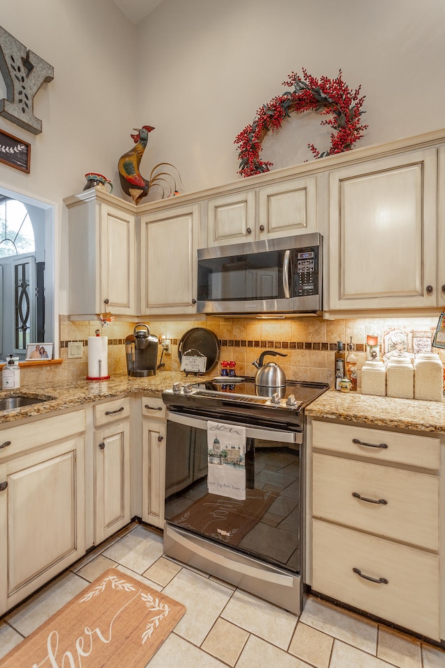 kitchen with backsplash, stainless steel appliances, a towering ceiling, and light tile patterned floors