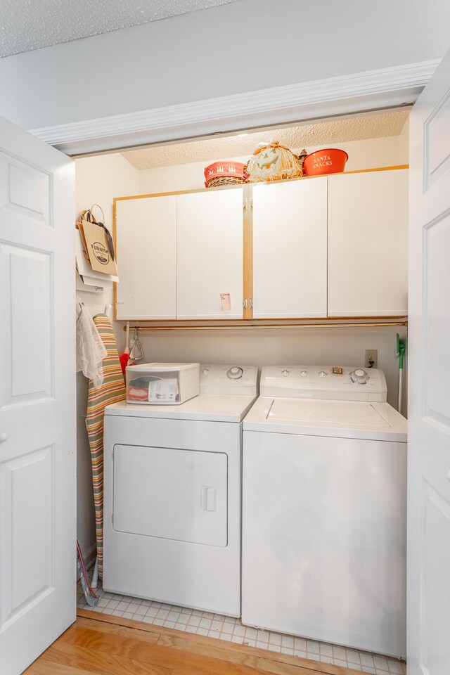 laundry area featuring cabinets, light hardwood / wood-style flooring, a textured ceiling, and washing machine and dryer