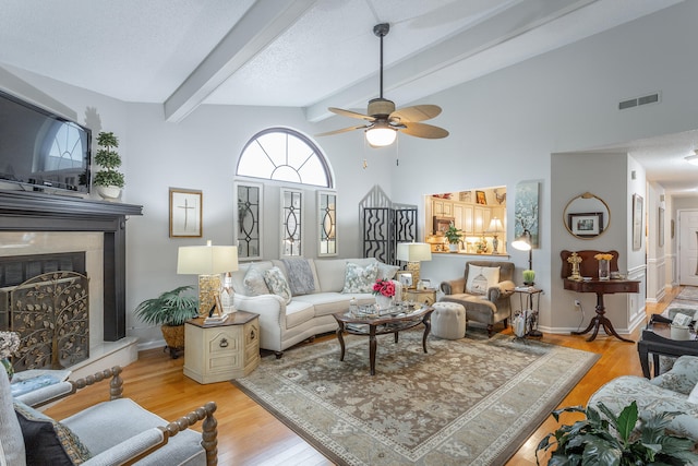 living room featuring light wood-type flooring, a textured ceiling, ceiling fan, beam ceiling, and high vaulted ceiling