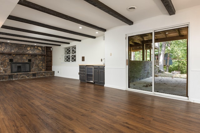 unfurnished living room featuring a stone fireplace, beam ceiling, dark hardwood / wood-style flooring, and beverage cooler