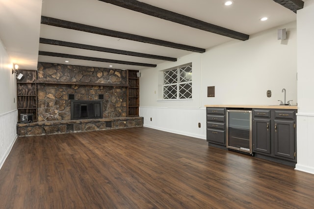 unfurnished living room featuring indoor wet bar, wine cooler, beamed ceiling, dark hardwood / wood-style floors, and a fireplace