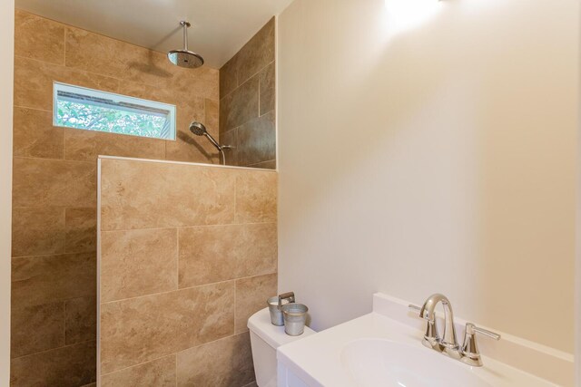 bathroom featuring a tile shower, toilet, and sink