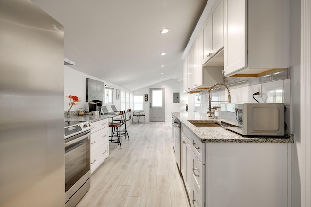 kitchen featuring light stone countertops, sink, lofted ceiling, white cabinets, and appliances with stainless steel finishes