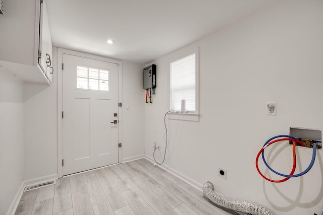 clothes washing area with cabinets, washer hookup, electric dryer hookup, water heater, and light wood-type flooring