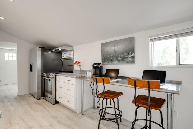 kitchen with stainless steel electric range, white cabinets, a kitchen breakfast bar, wall chimney range hood, and vaulted ceiling