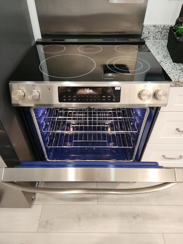 interior details featuring white cabinets, light stone counters, and stainless steel range oven