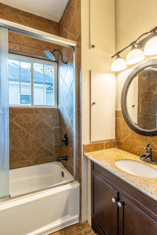 bathroom with a textured ceiling, bath / shower combo with glass door, and vanity