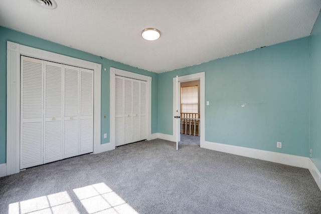 unfurnished bedroom with multiple closets, a textured ceiling, and light colored carpet