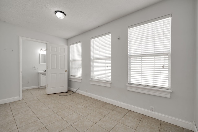 unfurnished bedroom with light tile patterned floors, connected bathroom, and a textured ceiling