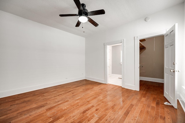 unfurnished bedroom featuring a textured ceiling, a spacious closet, a closet, ceiling fan, and light wood-type flooring