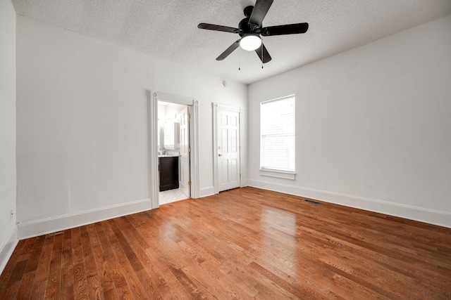 unfurnished bedroom with a textured ceiling, wood-type flooring, connected bathroom, and ceiling fan