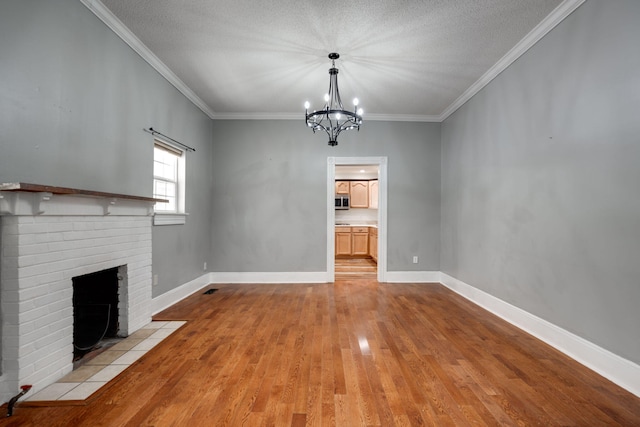 unfurnished living room featuring crown molding, a textured ceiling, light hardwood / wood-style flooring, a chandelier, and a brick fireplace