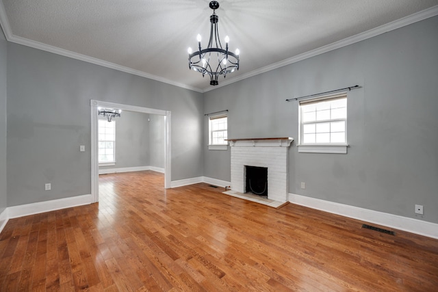 unfurnished living room featuring a textured ceiling, a fireplace, a notable chandelier, crown molding, and hardwood / wood-style flooring