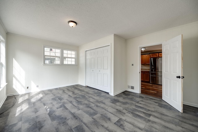 unfurnished bedroom with crown molding, light hardwood / wood-style floors, a closet, stainless steel fridge, and a textured ceiling