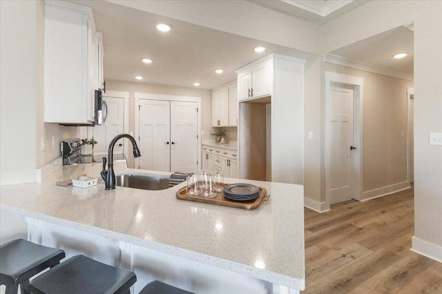 kitchen with crown molding, light hardwood / wood-style flooring, light stone countertops, white cabinetry, and kitchen peninsula