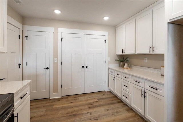 kitchen with white cabinetry, wood-type flooring, and light stone counters