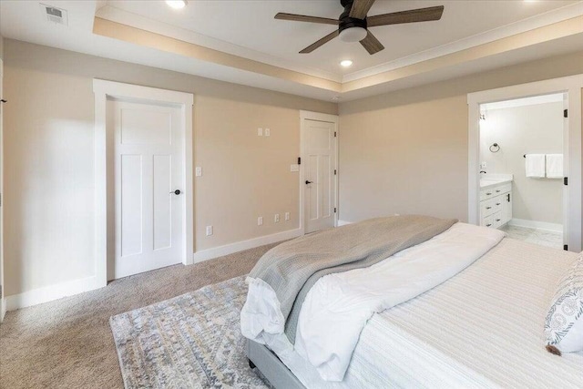 carpeted bedroom with a raised ceiling, connected bathroom, and ceiling fan