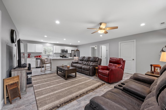 living room featuring ceiling fan, light hardwood / wood-style flooring, and sink