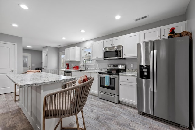 kitchen with a kitchen island, a kitchen bar, white cabinetry, stainless steel appliances, and light hardwood / wood-style floors