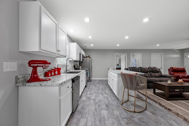 kitchen featuring sink, white cabinetry, appliances with stainless steel finishes, light stone countertops, and light hardwood / wood-style floors