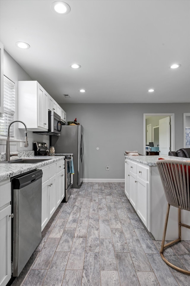 kitchen featuring appliances with stainless steel finishes, light hardwood / wood-style floors, white cabinets, light stone countertops, and sink