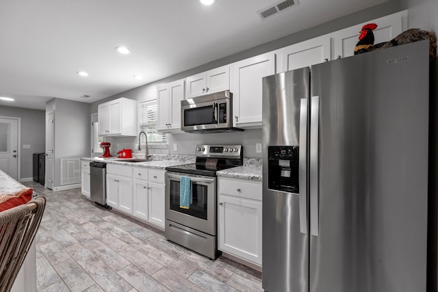 kitchen with light stone counters, white cabinets, appliances with stainless steel finishes, and sink