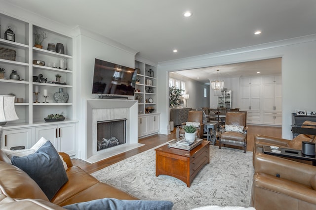 living room featuring built in shelves, light hardwood / wood-style flooring, ornamental molding, and an inviting chandelier