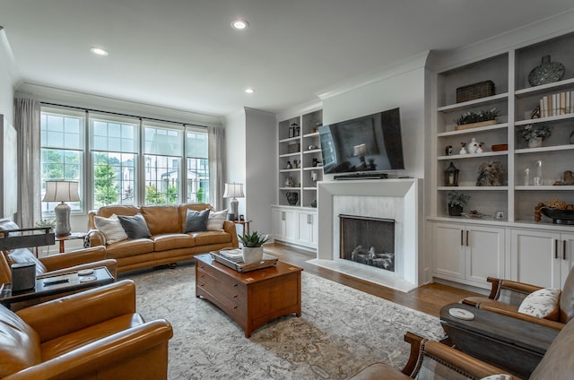 living room with built in shelves, light hardwood / wood-style floors, ornamental molding, and a fireplace