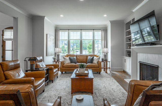 living room featuring a high end fireplace, ornamental molding, built in shelves, and light hardwood / wood-style floors