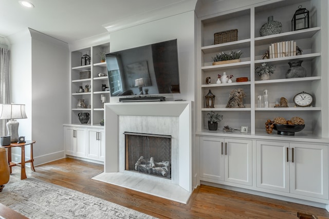 living room featuring a fireplace, crown molding, light hardwood / wood-style flooring, and built in features