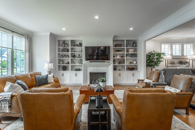 living room featuring built in shelves, light hardwood / wood-style flooring, ornamental molding, and a fireplace