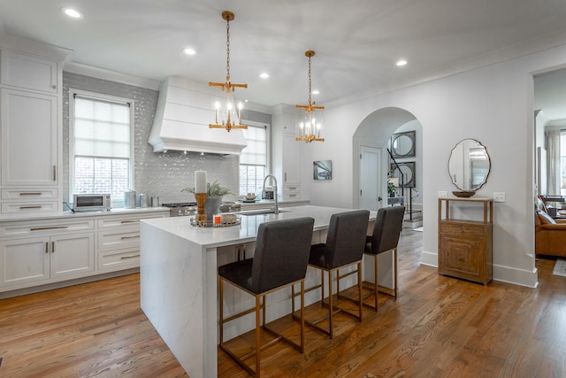 kitchen with light wood-type flooring, an island with sink, white cabinetry, and sink