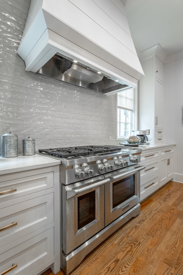 kitchen featuring range with two ovens, white cabinets, custom exhaust hood, and light hardwood / wood-style floors