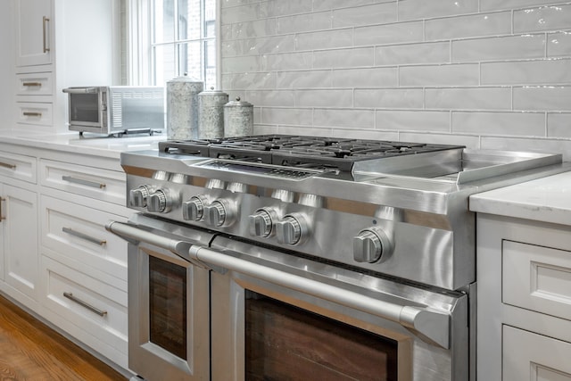 kitchen featuring white cabinetry, hardwood / wood-style floors, decorative backsplash, and double oven range