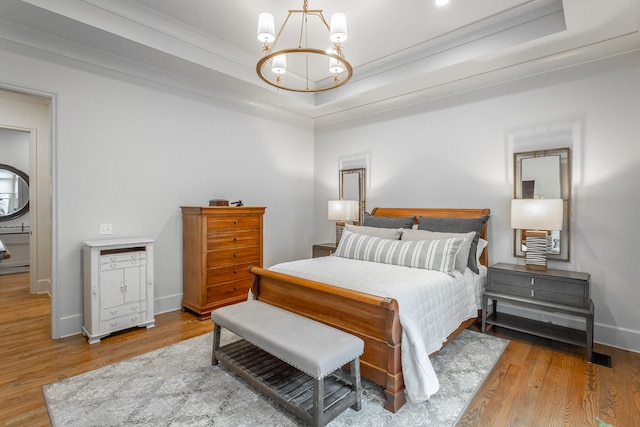 bedroom featuring a tray ceiling, light wood-type flooring, crown molding, and a notable chandelier