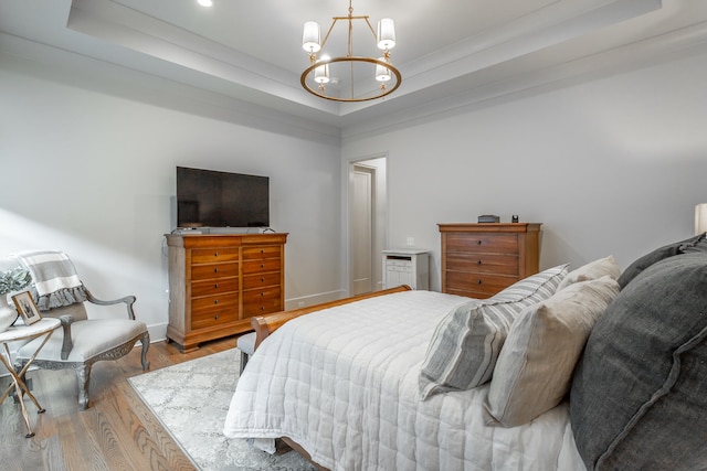 bedroom featuring ornamental molding, a chandelier, a tray ceiling, and light hardwood / wood-style floors