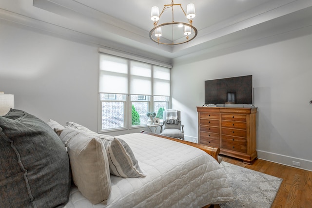 bedroom with a chandelier, hardwood / wood-style flooring, a raised ceiling, and crown molding