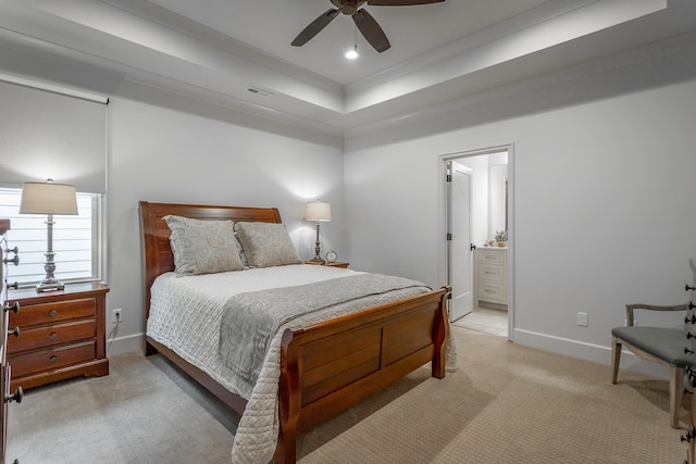 bedroom featuring light carpet, a tray ceiling, connected bathroom, ornamental molding, and ceiling fan