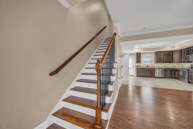 stairway featuring a tray ceiling, crown molding, hardwood / wood-style floors, and sink