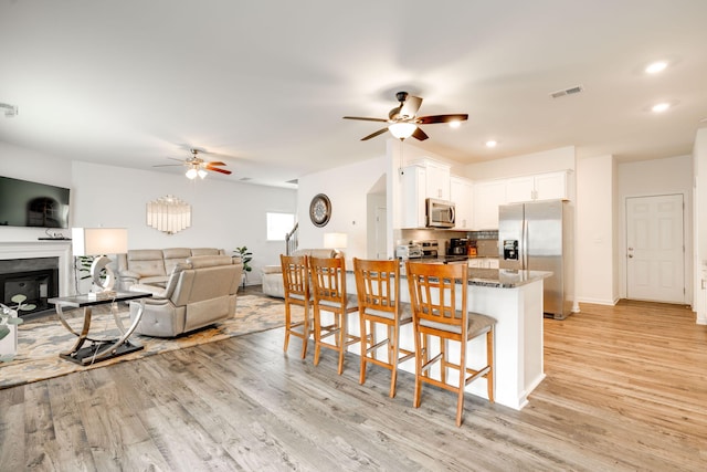 kitchen featuring appliances with stainless steel finishes, light hardwood / wood-style floors, white cabinetry, kitchen peninsula, and a breakfast bar area