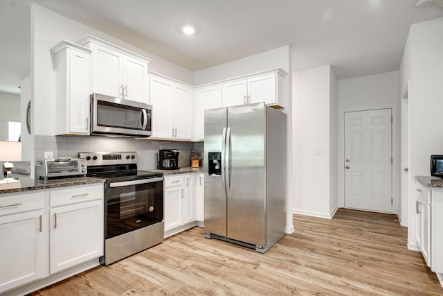 kitchen featuring white cabinets, stainless steel appliances, dark stone counters, and light hardwood / wood-style flooring