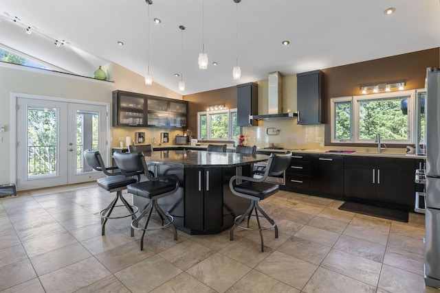 kitchen with a kitchen island, lofted ceiling, wall chimney range hood, and a healthy amount of sunlight