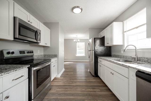 kitchen with light stone countertops, appliances with stainless steel finishes, sink, white cabinets, and dark hardwood / wood-style floors