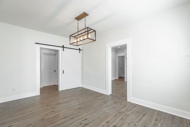 unfurnished dining area featuring an inviting chandelier, dark wood-type flooring, and a barn door