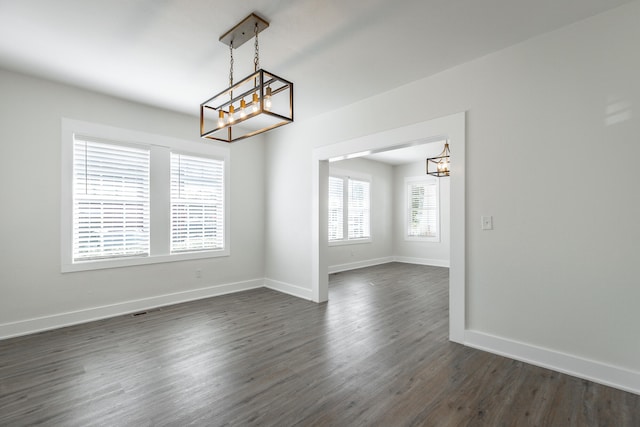 spare room with a notable chandelier and dark wood-type flooring